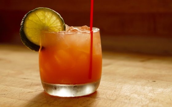 A single peach color drink in a tumbler glass adored with a lime wedge.