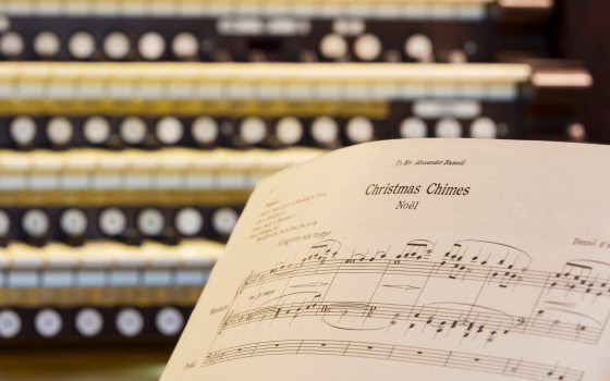 Closeup of an organ keyboard with sheet music for Christmas Chimes Noel in the right foreground.