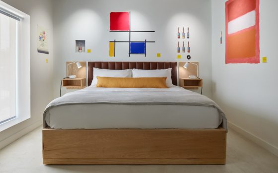 The inside of a hotel room, featuring a king bed and art painted on the walls.