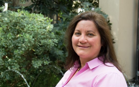A person in a pink button down shirt with long brown hair smiling at the camera.