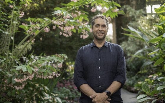 man with beard wearing a dark grey shirt smiling at the camera in a garden setting