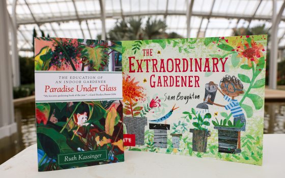 Two colorful books—entitled "Paradise Under Glass" and "The Extraordinary Gardener"—stand on a stone wall with a glimpse of tropical plants in the background, all beneath a glass ceiling.