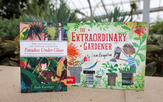 Two colorful books—entitled "Paradise Under Glass" and "The Extraordinary Gardener"—stand on a stone wall with a glimpse of tropical plants in the background, all beneath a glass ceiling.