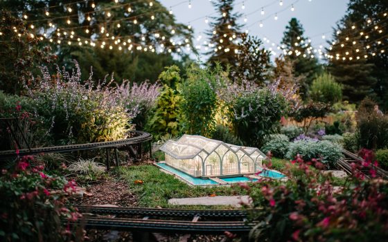 A model of a glass conservatory sitting in an outdoor model train display.