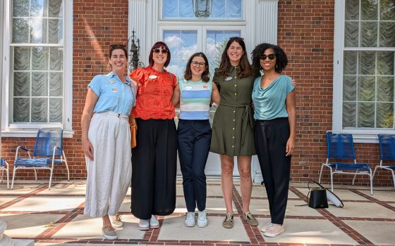 Five people standing shoulder to shoulder in front of a brick building, posing for the camera.