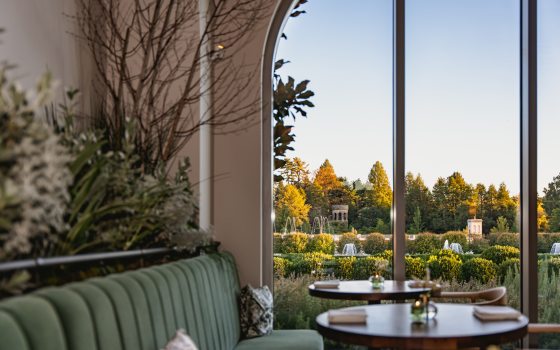 The interior of a restaurant featuring a sage green couch and tall arched ceilings. 