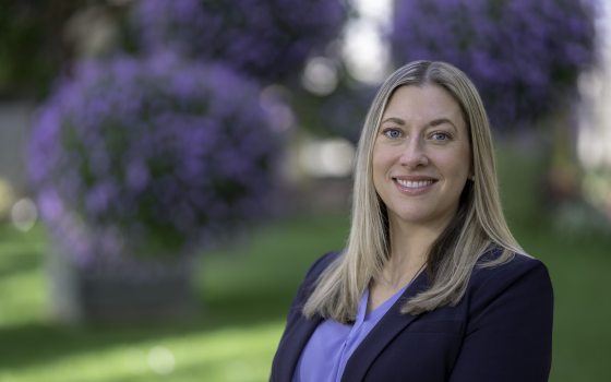 Lady with blonde hair wearing dark purple jacket and lavender shirt smiling at the camera