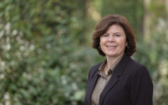 Lady with short brown hair wearing a brown jacket over a light brown dress shirt smiling at the camera