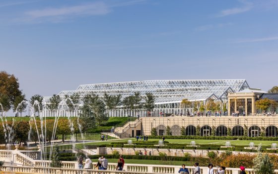 a landscape view of the West Conservatory, a steel and glass structure, amidst Longwood's Main Fountain Garden