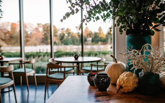A counter decorated with candles, gourds, and a large teal vase of greenery gives way to tables in front of arched windows overlooking a fountain garden.