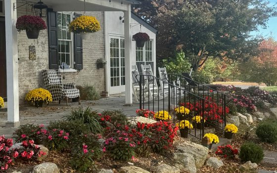 A side view of an old stone house, with blooming chrysanthemums lining the path in front of the porch.