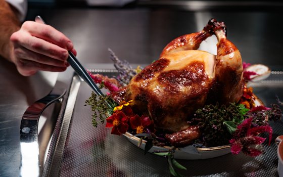 A person plating a whole roasted chicken on top of a bed of flowers. 