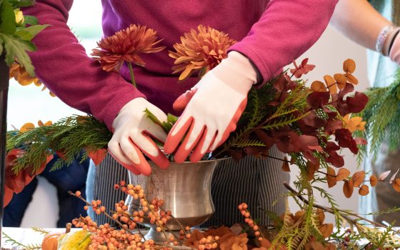 A person creating a floral arrangement in a silver vase.