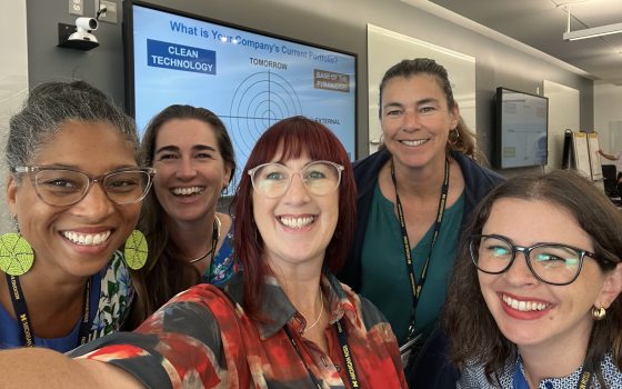 A selfie of 5 adults with a classroom in the background. 