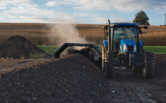 A blue tractor processes rows of compost in a green field