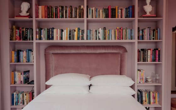 A rose colored hotel room featuring a bed surrounded by shelves of books. 