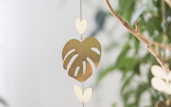 A windchime in the shape of a monstera leaf, hanging from a tree limb.