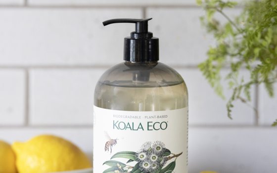 A container of handsoap on a black counter with a jar of lemons behind it.