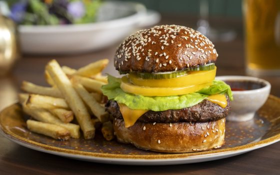 Closeup of burger with toppings on sesame seed bun, with fries on the side.