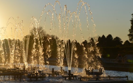 A row of fountains, spraying water up in the air, at sunset.