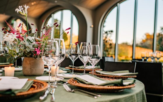 a round dining table set with a sage green table cloth, a bright flower arrangement, and wine glasses