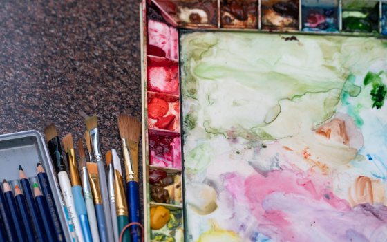 A watercolor and paint palette next to paint brushes.