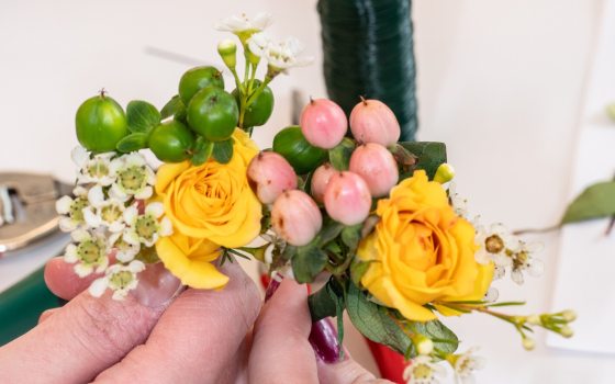 A persons hand creating a floral arrangement out of yellow and pink flowers. 