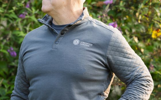 A person modeling a dark gray pullover with the Longwood Gardens logo on the upper left. 