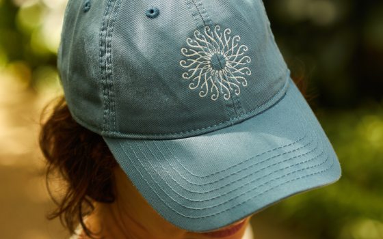 A person modeling a denim color hat with the Longwood Gardens rosette.