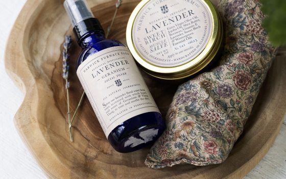 A wood tray filled with lavender bath products like a spray, soap, and balm.