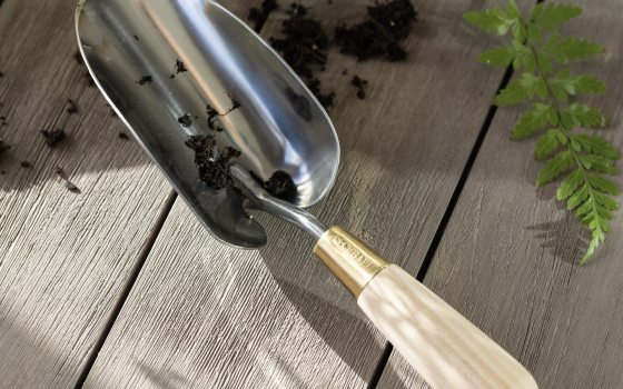 A stainless steel garden shovel with beige handle on a table.