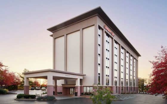 A hotel exterior, with Hampton Inn written at the top of the building in red. 