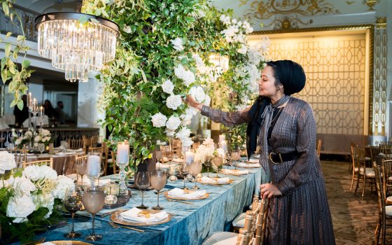 A person arranging a floral centerpiece next to an elegantly set table. 