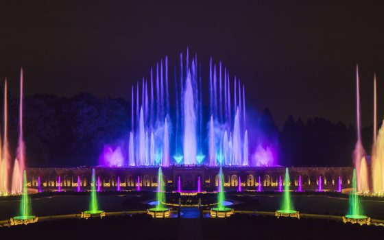 Evening in the Main Fountain Garden, with multi-colored jets of water in green, blue, purple, yellow and colors in between shooting into the dark sky