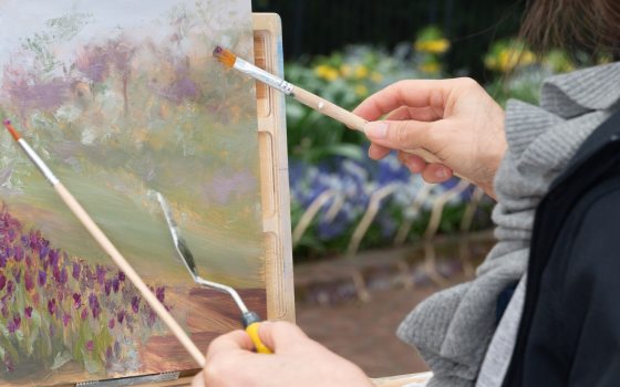 A person using paintbrushes to create a still life painting.