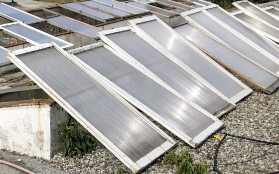 An outdoor, high-angle view of multiple cold frames, lying at a slight angle on a rough, gravel-covered ground or rooftop. 
