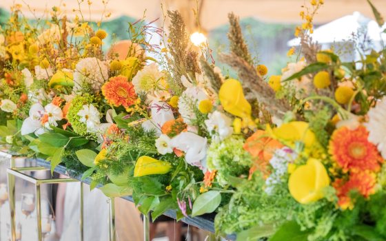 A tablescape of yellow, orange, and white flowers in tall mirrored vases.