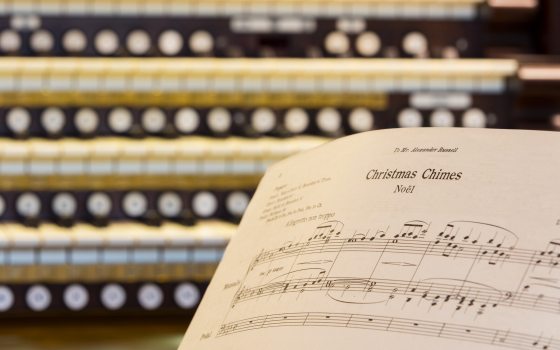 Closeup of an organ keyboard with sheet music for Christmas Chimes Noel in the right foreground.
