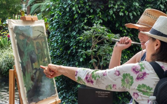 A close-up of two art students or artists pointing at and reviewing a landscape painting in progress during an painting class.