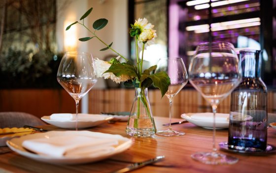 Set dining table with wine glasses, white plates, a napkin, a water bottle, and a small vase with a single white flower, suggesting a fine dining atmosphere.