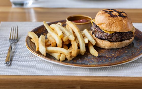 Hamburger and fries with sauce on dark brown plate.
