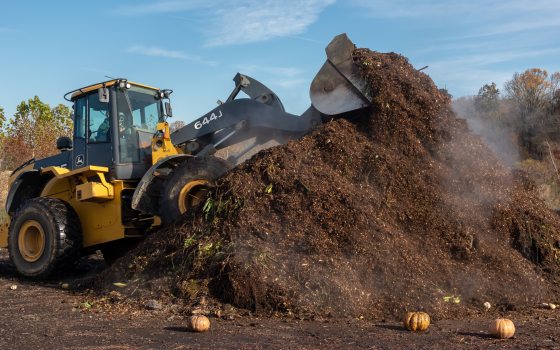 A yellow tractor on a steaming pile of dark brown composted soil.