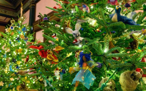 A vertical shot of a heavily decorated Christmas tree. The ornaments are unique, including a central needle-felted white rabbit with a red scarf, a figure with a blue fabric skirt, a felted blue bird, and various other whimsical animal ornaments.