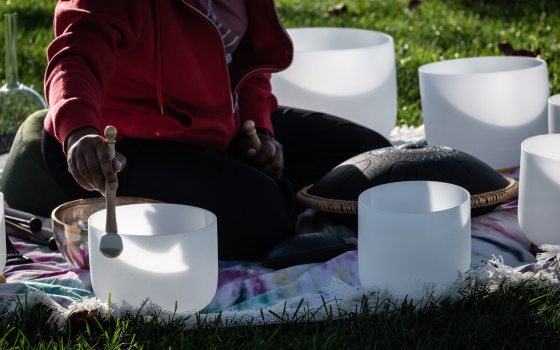 A person sitting outdoors on a blanket, surrounded by various instruments used for a sound bath or meditative practice.