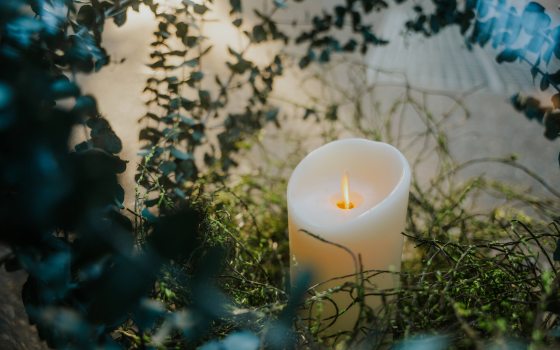 Closeup of glowing white pillar candle amid preserved floral material.
