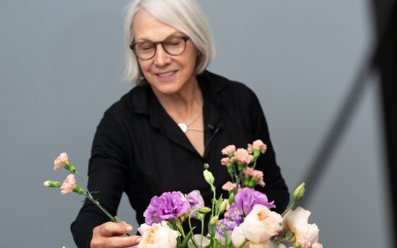 A person in a black shirt, with silver hair, arranging a floral design.