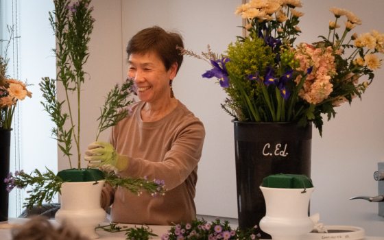 A person smiling behind a table while arranging florals.