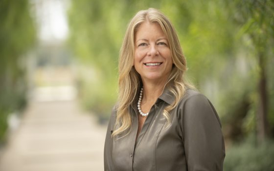 A person with blond hair, in a olive green dress shirt, smiling at the camera.