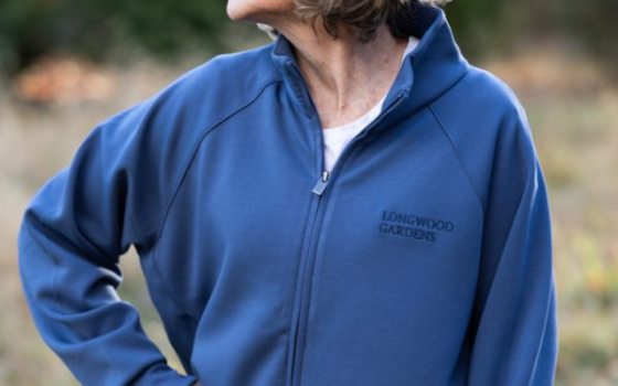 A person modeling a blue zip up sweatshirt with the Longwood Gardens logo on the left side.