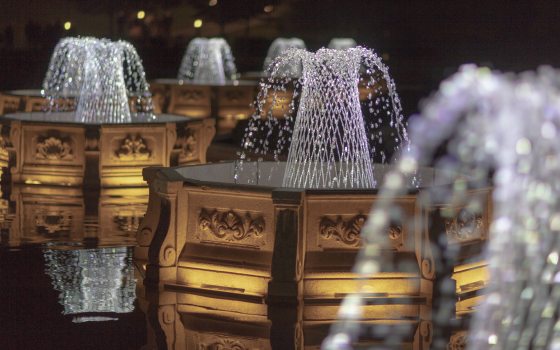Basketweave fountains in octagonal basins lit by sparkling white light against a black sky.